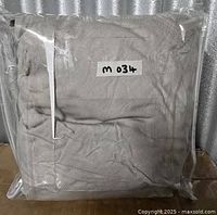 Sealed clear plastic bag containing folded grey cotton slipcover, label on exterior