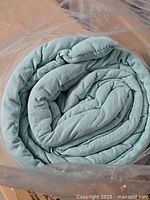 Rolled light aqua comforter inside plastic bag