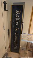 Full view of vertical black glass sign with gold lettering and gold border