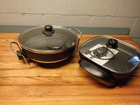 Both electric skillets with lids shown side by side