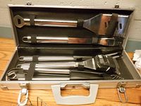 open aluminum case displaying five stainless steel grilling tools