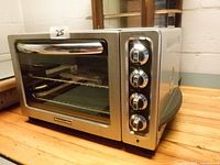 Front view of stainless steel KitchenAid convection toaster oven showing glass door, handle, control knobs and rack inside