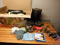 Entire lot displayed on wooden table including boxed hedge trimmer, boots, gloves, hose and accessories