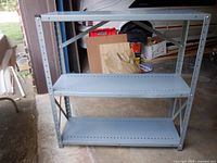 Front angled view of entire grey metal shelf unit showing three shelves and cross-bracing