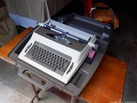 Typewriter resting on case lid atop stand