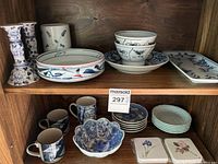 Full view of lot on shelves showing plates, bowls, mugs, candle holders, vase and coasters