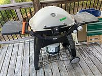 Front view of Weber gas grill on cart with propane tank and brush visible