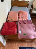 Five folded wool blankets on bed: two peach, red, mauve, dusty pink