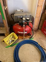 Front view of Porter-Cable pancake compressor showing gauges, label, attached hose and yellow tray of fittings