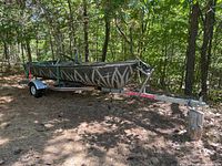 Profile view of aluminum rowboat on trailer in wooded area