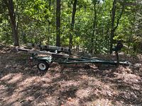 Side view of full green metal boat trailer in wooded area