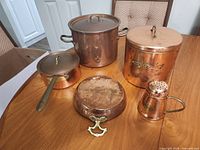 All five copper cookware and kitchenware pieces displayed on table with three lids