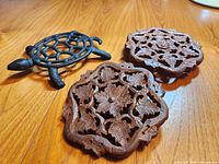 Group of two wooden floral trivets and one cast iron turtle trivet on wood surface