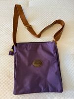 Front view showing purple nylon exterior, brown oval leather logo patch, tan adjustable strap