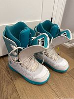 Front angled view of both boots showing white and teal color, laces, tongues