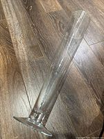 Full view of tall clear glass vase lying on wood floor