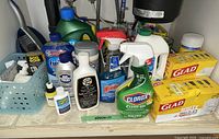 Overall view of cabinet contents showing cleaner bottles, basket, trash bags
