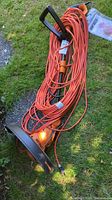 Electric string trimmer with coiled orange extension cord laid on grass