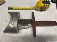 Side view of stereoscope showing metal hood with floral embossing, wooden slide, tape measure for scale