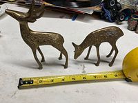 Two brass deer figurines beside tape measure