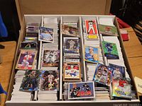 Four-row storage box partially filled with mixed sports trading cards, various sports and brands visible