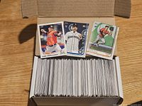 Open card storage box showing large stack of baseball cards with three sample rookie cards on top.