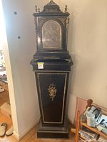 Full view of tall black ormolu mounted clock and pedestal
