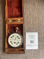 Front view of pocket watch in open wood box showing green enamel dial and complications