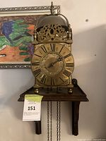 Front view of brass lantern clock on wall bracket showing dial, bell and bracket