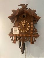 Front view of wooden Black Forest cuckoo clock showing dial, case carvings, weights and chains