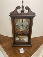 Front view of wooden case wall clock showing dial and pendulum
