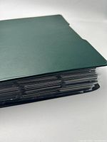 Closed green binder viewed from spine, showing thickness of filled pages
