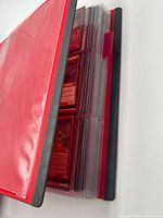 Red binder partially open showing stacked nine-pocket pages filled with trading cards