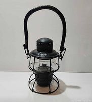 Front view of black railway lantern showing glass globe, wire guard, leather handle