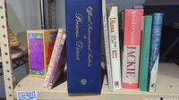 Shelf view showing all nine hardcovers arranged upright, titles for Princess Diana, Jackie Onassis and love poetry visible