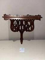 front view of carved mahogany wall shelf showing pierced scrollwork and drop finial