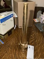 Full view of brass fire hose nozzle standing upright on table