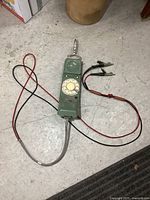 Full view of green rotary lineman phone with attached red and black leads and alligator clips on floor