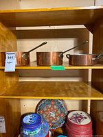 Front view of three copper cookware pieces on shelf