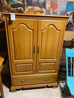 Front view of oak entertainment cabinet showing double doors, crown moulding, brass-tone hardware