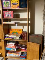 Shelf and cabinet showing multiple board games including TriBond, ThinkBlot, HedBanz, Arch Rival, Battleship, Mastermind and others