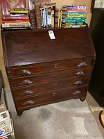 Front view of closed secretary desk showing four drawers and drop-front