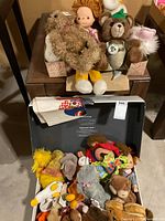 Assorted stuffed animals and doll on table and inside suitcase