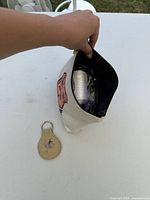 Hand opening canvas pouch showing beading thread spool and bead bags, keychain placed outside