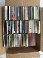 Open cardboard box filled with rows of CD jewel cases