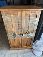 Front view of medium oak two-door cabinet with decorative stained glass panels and metal knobs, wrapped in plastic
