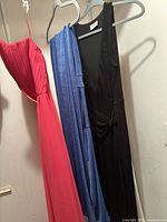 Front view of three dresses on hangers: pink/peach, blue, black