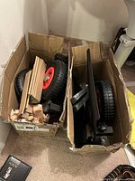 Two open boxes showing drywall dolly parts including red-hub pneumatic wheels and black steel frame sections
