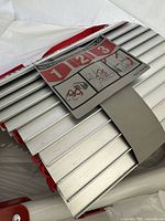 Close view of folded aluminium ladder rungs with red straps and instruction label