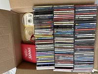 Open box showing stacks of music CDs, two blank CDs, and red zippered case